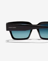 Lentes de sol unisex Hawkers, modelo Mate, con montura cuadrada negra y cristales degradados de azul a transparente.