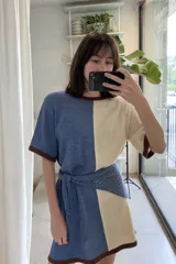 Vestido corto tejido artesanalmente en hilado azul y beige, con cuello redondo y mangas cortas con terminaciones en marrón. Incluye cinturón tejido.