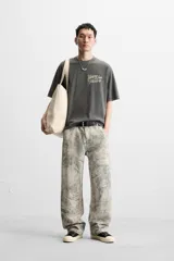 Camiseta gris oscuro con efecto lavado, cuello redondo y manga corta. Tiene un bolsillo en el pecho y estampados en el frente y la espalda.