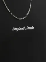 Buzo negro de manga larga con cuello redondo y calce relajado. Presenta un pequeño bordado en el pecho con el texto "Originals Studio" en cursiva blanca.