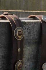 Cinturón marrón de cuero vacuno encerado, con hebilla metálica dorada y apliques de monedas metálicas con diseño floral.