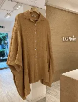 Camisa celeste de lino con corte amplio, cuello clásico, cierre frontal con botones de nácar y bolsillos laterales invisibles.