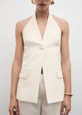 Chaleco largo color crema con cuello halter, espalda abierta, botón joya y bolsillos delanteros.
