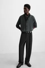 Pantalón negro de corte amplio confeccionado en tejido con mezcla de viscosa. Presenta cintura elástica, pliegues en la parte delantera, bolsillos laterales y traseros de vivo. Cierre frontal con cremallera y gancho metálico oculto.