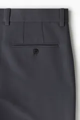 Pantalón de vestir gris oscuro, tobillero, de corte slim fit, con cierre de botón, bolsillos laterales y traseros ribeteados con botón.