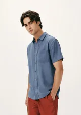 Camisa celeste de manga corta con cuello clásico, cierre frontal con botones y bolsillo de parche en el pecho. Corte recto.