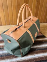 Bolso de lona azul con detalles en cuero marrón, doble asa de mano y correa bandolera ajustable. Incluye un neceser haciendo juego con cierre y logo de caballo bordado.