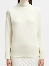 Buzo de lana y cachemira color crema, con cuello alto y logo de la marca bordado en el frente.