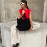 Cartera tipo tote bag confeccionada en lona de color negro. Presenta un diseño funcional con doble asa de mano, un compartimento principal espacioso y un bolsillo frontal con solapa.