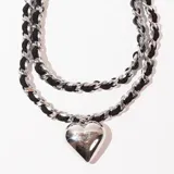 Gargantilla de doble cadena, una de eslabones plateados y otra de cordón trenzado negro, con dije de corazón plateado.
