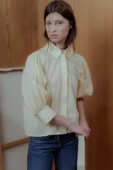 Camisa color crema de algodón, con cuello clásico, cierre frontal con botones y mangas cortas abullonadas.
