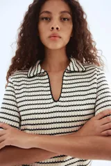 Top de punto con textura a rayas horizontales en blanco y negro. Tiene cuello camisero abierto, mangas cortas y corte holgado.