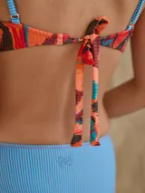 Top de bikini con estampado abstracto en tonos naranja, marrón, negro y blanco. Tirantes finos con diseño a rayas verticales de colores.