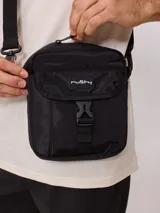 Bandolera gris de nylon con correa negra ajustable y logo Rusty estampado en negro.