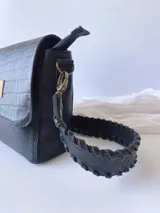 Cartera negra fabricada en cuero con forro de tela, bolsillo interior y correa corta trenzada.
