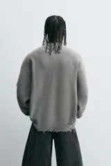 Sweater gris de punto con cuello en V, manga larga y terminaciones irregulares con efecto desgastado.
