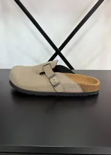 Zuecos beige con hebilla metálica ajustable, plantilla de corcho y suela de goma negra.