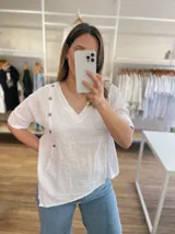 Blusa celeste de lino con cuello en V, mangas cortas con dobladillo y cierre lateral con botones de madera.