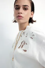 Remera blanca de algodón con cuello redondo y mangas cortas. Presenta un diseño calado en el frente.