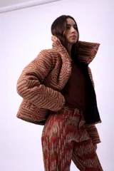 Campera corta con estampado abstracto en tonos marrones y beige, cuello alto, cierre frontal con botones a presión, bolsillos delanteros y bordado negro con las iniciales CP. Forro interior y relleno liviano de guata.