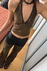 Top marrón de cuero ovino vintage con cuello halter, espalda descubierta y cierre con lazos. Presenta detalle artesanal de cutouts y pasamanería en negro alrededor del cuello.