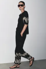 Pantalón culotte negro de lino y viscosa con bordados florales en el ruedo. Tiene tiro medio, cintura con trabillas, bolsillos laterales y cierre frontal con cremallera y botón.