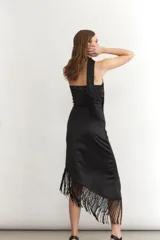 Vestido midi sin mangas color turquesa, con escote strapless y detalle de nudo frontal. El ruedo presenta un corte asimétrico con flecos negros largos.