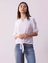 Blusa blanca de tejido texturado con cuello redondo, escote en V con aplique metálico y mangas 3/4 con puños elásticos. El ruedo se ata con un nudo.