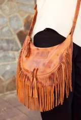 Cartera bandolera de cuero color marrón con flecos largos en la parte inferior y correa ajustable.