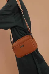 Bandolera color mostaza de simil cuero, con tres cierres principales, cierre delantero y bolsillo trasero. Incluye correa ajustable.