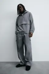 Pantalón cargo gris con textura acanalada, corte relaxed fit, cintura elástica con pliegues frontales, bolsillos laterales tipo cargo con solapa, bolsillos frontales y traseros de vivo, cierre frontal con cremallera y botón.