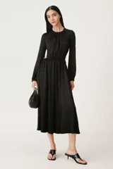 Vestido midi negro de cuello redondo y manga larga abullonada con puños. Tiene cintura elástica y detalle de espalda descubierta. El cierre es con botón en el cuello.
