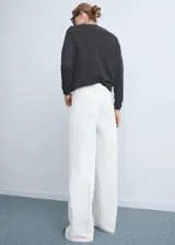 Pantalón de jeans blanco, tiro alto, corte wideleg (pierna ancha) y largo. Presenta bolsillos de parche en la parte delantera y bolsillos traseros.