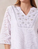 Blusa blanca de broderie con cuello a la base y escote en V. Apliques de brillos y piedras nacar en la parte delantera.