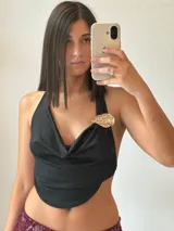 Top negro con escote drapeado, espalda descubierta y detalle de broche dorado en el hombro.