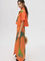 Camisa crop verde con estampado abstracto en tonos naranja y celeste, de mangas cortas y cuello camisero. Confeccionada en viscosa.