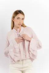 Blusa color rosa pálido de algodón, con cuello alto con lazo y mangas largas con volados.