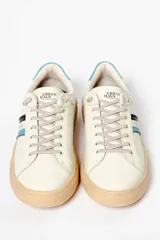 Zapatillas deportivas de cuero sintético color blanco hueso, con suela marrón claro y detalles en azul y negro.