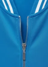 Chaqueta deportiva azul con cierre frontal, cuello redondo y terminaciones con rayas blancas en cuello, puños y ruedo.