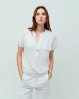 Remera blanca de lino con cuello mao, media cartera con broches metálicos níquel, caja boxy, manga japonesa, bolsillo plaqué delantero y ruedo redondeado escalonado con lavado fade teñido en frío.