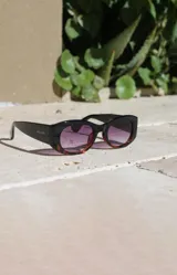 Lentes de sol con montura gruesa de acetato color negro y marrón carey, con lentes degradadas de violeta a naranja.