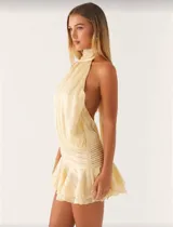 Minivestido color crema, con cuello halter, espalda descubierta, cintura elastizada y falda con volados.