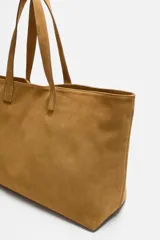 Bolso tipo shopper color marrón claro, fabricado en piel con acabado serraje. Tiene un compartimento principal con cierre imantado y un bolsillo interior con cremallera. Cuenta con dos asas de mano fabricadas en piel.