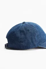 Gorra de denim azul con ojales bordados en la parte superior, trabilla ajustable con hebilla de metal en la parte trasera y cinta antitranspirante de algodón.