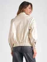Campera bomber color beige de eco cuero, marca Elan. Tiene cuello con solapa y botón a presión, cierre metálico central, bolsillos delanteros con solapa y botón a presión, y ruedo trasero elastizado.