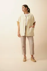 Chaleco color crema de lana sin teñir, corte recto, con cuello y solapa pronunciadas, broches a presión y bolsillos ojal.