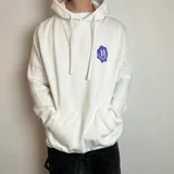 Canguro blanco con capucha y cordones ajustables. Estampado en la espalda con diseño de tablero de ajedrez en color violeta, un smiley face distorsionado y la frase "Good Vibes" en tipografía cursiva.