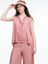 Camisa gris sin mangas confeccionada en viscosa teñida en frío, con efecto gastado. Tiene cuello clásico, cartera oculta y ruedo irregular más largo en los laterales.