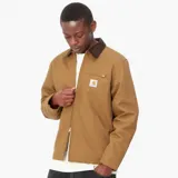 Chaqueta de estilo workwear en color tostado, con cuello de pana en contraste marrón oscuro. Cuenta con cierre frontal de cremallera, un bolsillo con cierre en el pecho y el parche con el logo de la marca en el frente.