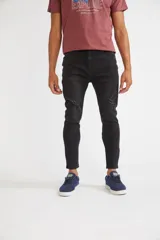 Pantalón jean negro de corte carrot, suelto en la cintura y ajustado en el tobillo, con roturas en las rodillas y logo bordado.